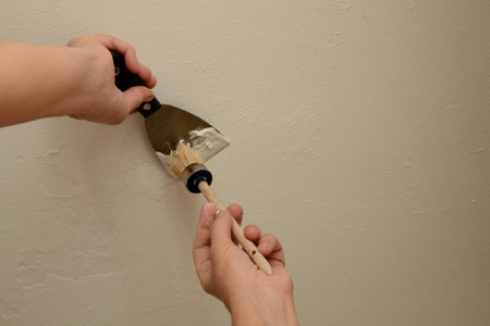 Woman plasterer repairing the wall with putty. With a brush, the master collects putty from the tool. Close-up, copy space.の写真素材