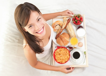 Woman having breakfast in bed. Big continental breakfast. Asian caucasian woman smiling looking at...
