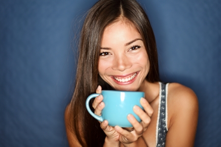 Woman smiling drinking tea on blue background. Young beautiful multiracial Asian / Caucasian female model joyful.の写真素材