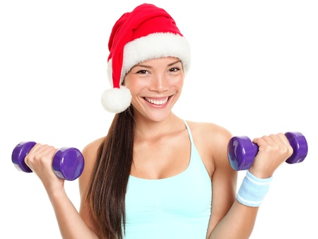 Christmas fitness sport woman wearing santa hat doing gym excersise training arms lifting dumbbells. Mixed race Chinese Asian Caucasian female fitness model isolated on white background.の写真素材