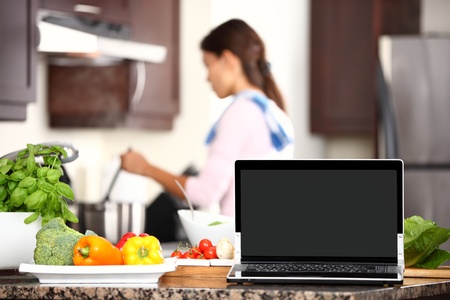 cooking and computer laptop concept. Blank pc monitor screen in focus with cooking woman in kitchen.の写真素材