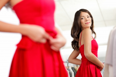 Girl trying dress in looking in mirror cheerful and happy. Cute beautiful mixed race Asian / Caucasian young woman oin red dress.の写真素材