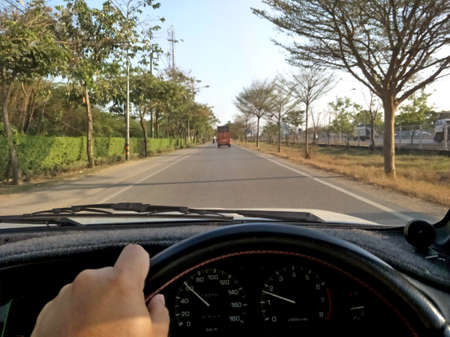 Hands driving a car on on steering wheel of a car and empty asphalt road.