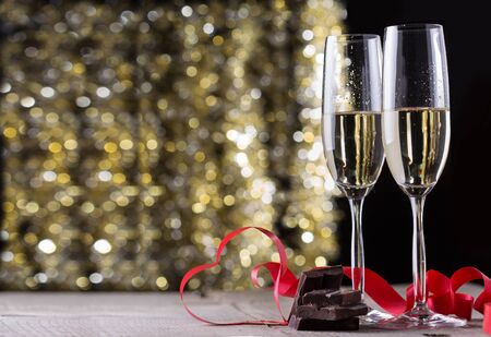 Champagne glasses and heart shape ribbon in front of gold glitter backgroundの写真素材