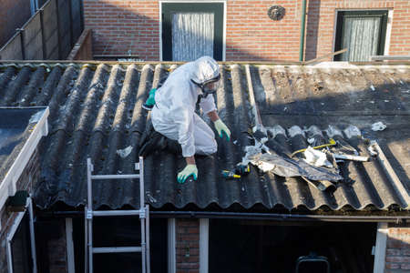 Professional asbestos removal. Men in protective suits are removing asbestos cement corrugated roofingの写真素材