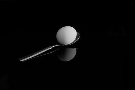 An egg on a spoon. With reflection on a black backgroundの写真素材