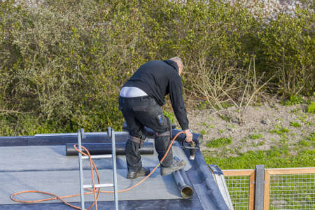 A roofer installing roofing felt with a propane blowtorch. Heating and melting bitumen roofing felt.