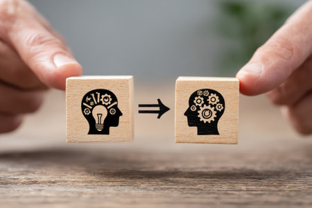 Two small wooden blocks, one with an idea icon, the other with a gear icon, held by hands, connected by an arrowの素材
