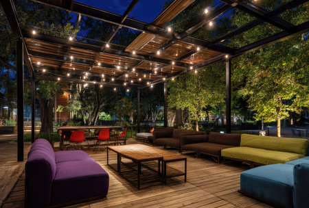An outdoor lounge area is illuminated by string lights at night. The scene features contemporary furniture, including sofas and tables. The color palette includes shades of brown, green, and purple, creating a relaxed atmosphere. This image could be used for commercial purposes, such as advertising or editorial content.の素材