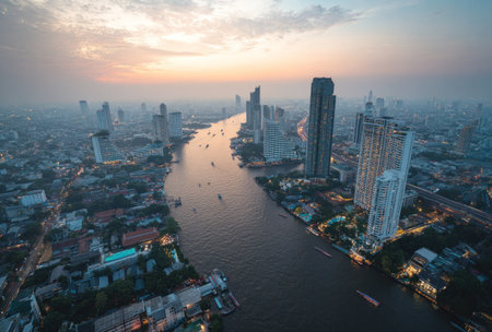 An aerial photograph captures a cityscape bisected by a river at sunset. Buildings of varied heights and designs line the waterways. The sky displays hues of yellow and orange. This image could serve various purposes like illustrating urban planning, or tourism related content.の素材