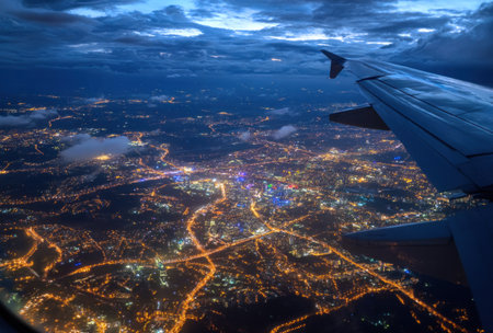 An aerial perspective shows a city sprawling beneath a darkened sky at night. The image captures the scene with an airplane wing visible, displaying a network of lights. The composition and lighting create a sense of scale and offer a commercial appeal that can be utilized for various creative projects.の素材