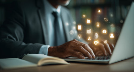 A person in a suit is working on a laptop. Illuminated icons representing digital communication and technological processes are overlaid on the image. The setting appears to be indoors with soft lighting. Suitable for articles about technology, business, and modern communication.の素材