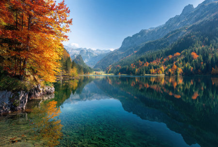 A scenic landscape presents a tranquil lake reflecting the surrounding mountains and vibrant autumn foliage. The composition features rich colors, including shades of green, orange, and blue. This image displays a natural outdoor environment with clear lighting, suitable for various editorial and commercial applications.の素材
