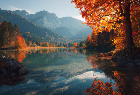 This image showcases a scenic autumn landscape. The central focus is a tranquil lake reflecting the sky and surrounding mountains. Vivid colors of the season are visible, with orange and yellow foliage. This composition could be used for various projects, including editorial features or commercial illustrations.の素材