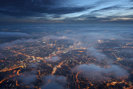 An aerial perspective showcases a city illuminated with countless lights under a partly cloudy sky. The photograph displays a multitude of buildings, streets, and infrastructure. This image, with its dramatic lighting and cool tones, could be used for various commercial or editorial purposes.の素材