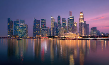 A cityscape at dusk displays towering skyscrapers reflecting in tranquil water. The scene features a blend of blues and purples with subtle highlights. The composition showcases a horizontal arrangement, with the buildings set against a colorful sky. This image could be suitable for various commercial or editorial uses.の素材