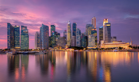 A panoramic view showcases a modern city skyline at dusk, illuminated by the warm glow of the setting sun. The composition highlights numerous tall buildings reflecting in the calm water. The scene features a blend of architectural designs and could be suitable for various commercial or editorial applications.の素材