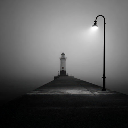 A grayscale image showcases a lighthouse and a lamppost against a misty background. The scene, captured in a monochrome style, features a strong contrast of light and shadow. It suggests a maritime environment, possibly at dusk or dawn. This image could be used for various editorial and commercial purposes.の素材