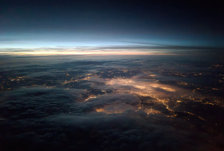 An aerial perspective showcases a cityscape illuminated below a layer of clouds at dusk. The image presents a color palette of deep blues, oranges, and grays. The composition is wide, with a focus on natural lighting. It could be useful for editorial articles and commercial designs.の素材