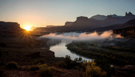 A tranquil landscape captures a river winding through a canyon at sunrise. The scene showcases mountain silhouettes, morning fog, and a warm color palette. Natural light illuminates the valley. This image could be used for editorial and commercial projects, illustrating nature and travel concepts.の素材