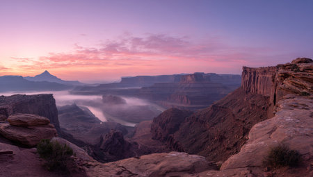 An expansive landscape showcases a canyon vista at dawn. Pink and purple hues color the sky above rocky cliffs and a valley filled with fog. The scene exhibits a natural composition and soft lighting, suitable for various editorial and commercial applications. The image offers a sense of vastness.の素材