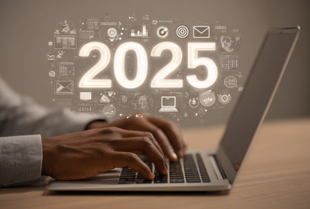 A person's hands are shown typing on a laptop, with a glowing 2025 graphic hovering above. The image displays a soft, neutral color palette with a focus on digital elements. The composition suggests an environment of innovation. It could be useful for illustrating technology or future-oriented content.の素材