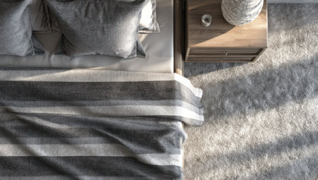 An overhead shot depicts a contemporary bedroom setting, focusing on a bed with striped bedding and plush pillows. The image showcases neutral tones, including grays and whites, with soft textures and natural lighting. This composition suits commercial applications, illustrating home decor and interior design concepts.の素材