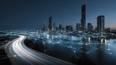A nighttime cityscape showcasing modern architecture and digital network connections. The image features illuminated skyscrapers set against a dark blue sky, with a road curving towards the city. The composition uses a low-angle perspective, creating a sense of depth and scale, suitable for various commercial applications.の素材