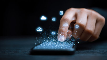 A hand interacts with a smartphone, surrounded by illuminated data icons and particles. The scene is set against a dark backdrop, creating contrast and emphasizing the glowing elements. The composition suggests digital connectivity and technology use. Suitable for articles or advertisements related to communication and technology.の素材