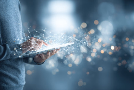 A person is interacting with a tablet computer. The image features a network of connected lines and particles. The visual elements have a blue color palette with bokeh effects. The composition emphasizes technological themes. This image is suitable for various commercial applications.の素材