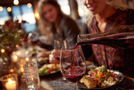 Two people are seen at a table as wine is poured into a glass. The scene has soft, warm lighting. The image captures a social gathering, with food and drinks. It could be used for various commercial purposes, advertising restaurants or lifestyle products. The image highlights dining and social activity.の素材