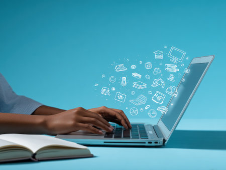 A person types on a laptop computer with a display of sketched icons over a vibrant blue backdrop. The image showcases the hands and keyboard of the device, alongside an open book. This visual composition, featuring cool tones and focused lighting, lends itself well to technology, education and business themes for editorial and commercial applications.の素材
