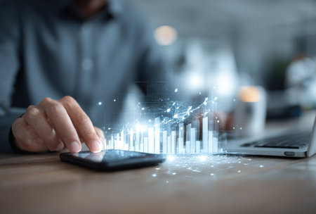 A person's hand interacts with a smartphone, with a digital chart floating above the device. The composition features a shallow depth of field, with soft lighting and a focus on the glowing graphic. This image could be used for articles, reports, or marketing materials related to business, technology, and finance.の素材