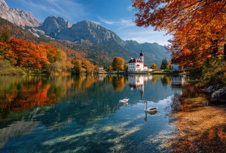 A vibrant landscape showcases a tranquil lake reflecting a castle and colorful foliage. Mountains frame the background under a bright blue sky. The composition features rich autumn hues and a serene ambiance, suitable for various editorial and commercial applications.の素材