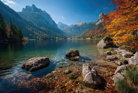 A landscape featuring a calm lake surrounded by mountains and trees displaying vibrant autumn colors. The image showcases clear water, rugged rocks, and a bright blue sky. This setting may be suitable for illustrating natural beauty, travel destinations, or outdoor adventure themes for various editorial or commercial purposes.の素材