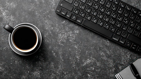 An overhead view displays a black coffee cup on a saucer, positioned near a keyboard on a dark textured surface. The scene features high contrast with stark shadows, emphasizing the coffee's dark color and the keyboard's form. This setup would be suitable for commercial and editorial content, emphasizing themes of work and leisure.の素材