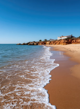 Sunny beach with waves, light beige sand, and distant buildingの素材