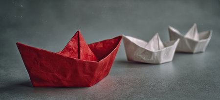Red origami boat leading two white origami boatsの素材