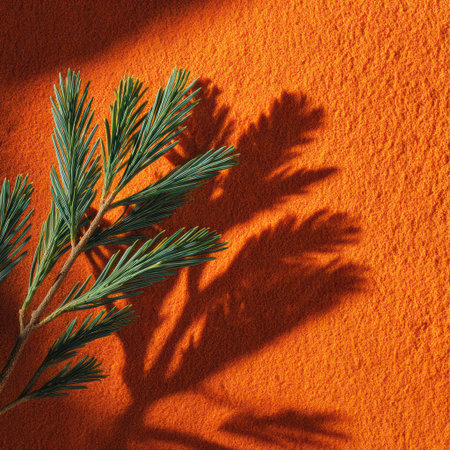 A green sprig with delicate leaves casts a strong shadow on an orange textured surface. The image exhibits high contrast with dramatic lighting. The composition is simple, emphasizing the natural forms and rich color palette. Suitable for various commercial and design applications.の素材