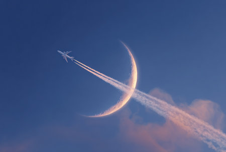 An airplane streaks across a dark blue sky, its vapor trail intersecting with the crescent moon. The image displays a unique composition, utilizing the juxtaposition of the aircraft and celestial body. It features soft lighting and could be used for conceptual art, educational materials, or projects exploring flight.の素材