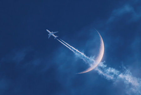 An airplane streaks across a dark blue sky, its vapor trail contrasting with the crescent moon. The composition highlights the aircraft's movement. The image employs soft lighting. This scene is suitable for use in travel, transportation, or conceptual projects to evoke feelings of adventure.の素材