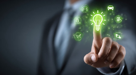 A person in professional attire touches a glowing lightbulb icon surrounded by other icons, suggesting innovative ideas. The image utilizes digital effects with green hues against a dark background, and an out-of-focus background. This type of image could be used in various commercial projects or editorial contexts to represent technology or business.の素材