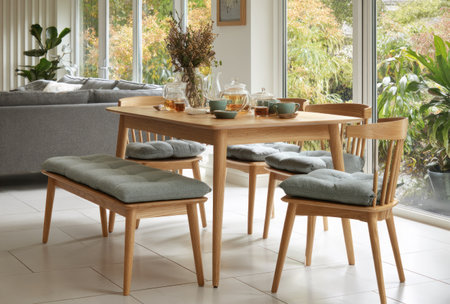 A wooden dining table and chairs are arranged in a well-lit space. The scene showcases neutral tones with cushions, and sunlight. The composition may be suitable for illustrating home decor, lifestyle, or commercial interior design themes. The image displays a clean and inviting aesthetic.の素材