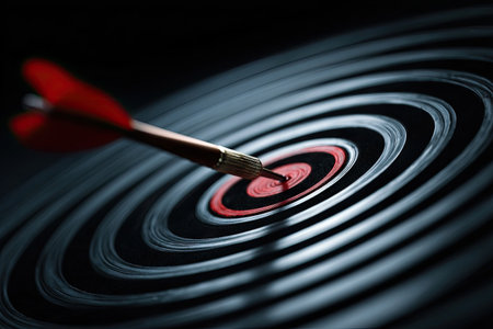 A close-up view depicts a dart hitting a target, focusing on the center ring. The image showcases a dark, circular pattern with concentric lines, highlighting the red bullseye. The composition features sharp focus and a shallow depth of field, suitable for illustrating concepts of achievement and success. Ideal for business-related articles or presentations.の素材