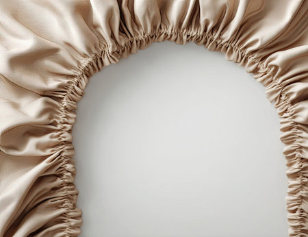 A close-up view presents a beige fitted sheet, with ruffled edges. The smooth fabric contrasts with the folded detail of the sheet. The color palette is warm and neutral, providing a sense of comfort. This image could be used for various commercial projects related to textiles and home decor.の素材