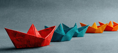 A formation of colorful paper boats stands out on a gray background. The scene showcases vibrant primary colors arranged in a row. The simple composition and soft lighting suggest a studio environment. This image could be used for various commercial or illustrative purposes.の素材
