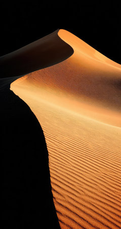 A close-up view presents a sculpted sand dune with distinct textures and shadows. The warm, earthy tones of the sand contrast dramatically with the dark background. The image, with its dramatic lighting and strong composition, is suitable for editorial or commercial applications, conveying a sense of serenity or mystery.の素材