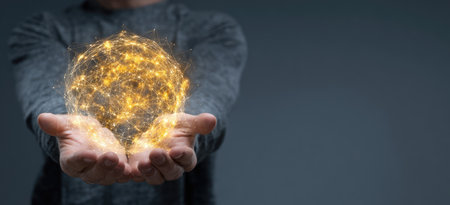 A person is holding a luminous, golden sphere in their cupped hands. The scene features a shallow depth of field, highlighting the bright orb against a blurred grey backdrop. The lighting is soft and diffused, creating a sense of wonder. The image is suitable for various commercial uses related to technology or abstract concepts.の素材