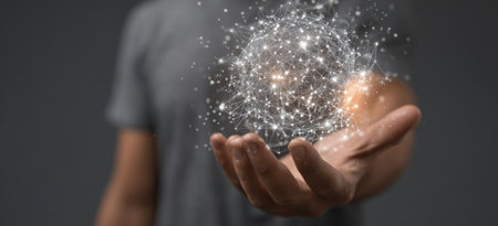 A person's hand is outstretched, holding a glowing sphere composed of interconnected particles. The image features a shallow depth of field, with soft lighting illuminating the subject against a blurred background. This visual could be used in various commercial applications related to technology or data visualization.の素材
