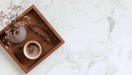 An overhead shot showcases a wooden tray holding a coffee cup, flowers, and a twig, set against a marble surface. The arrangement features warm wooden tones, creating a cozy contrast with the bright background. The composition is suitable for various commercial uses, including lifestyle and design projects.の素材